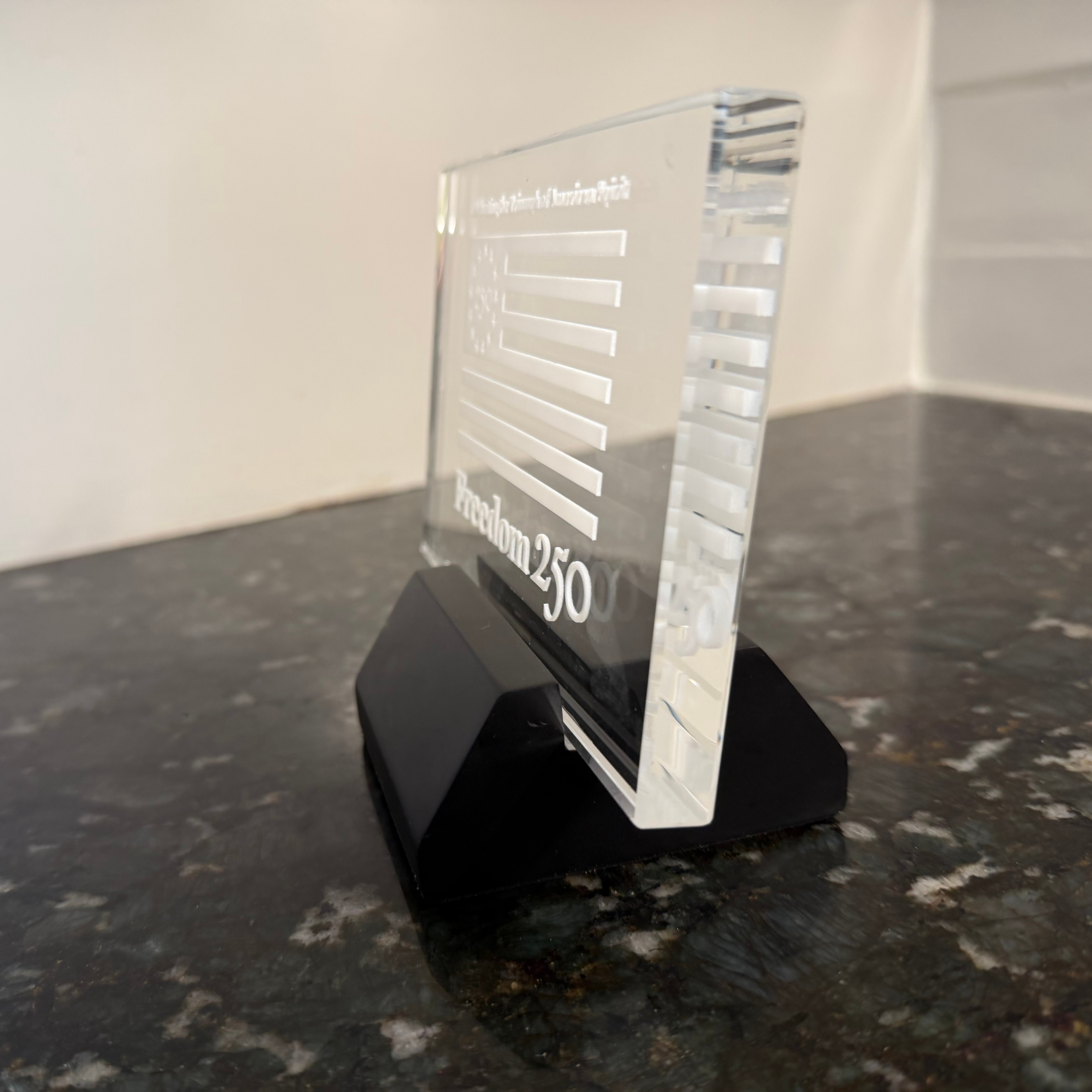 Clear glass award on a black stand with text on a marble surface
