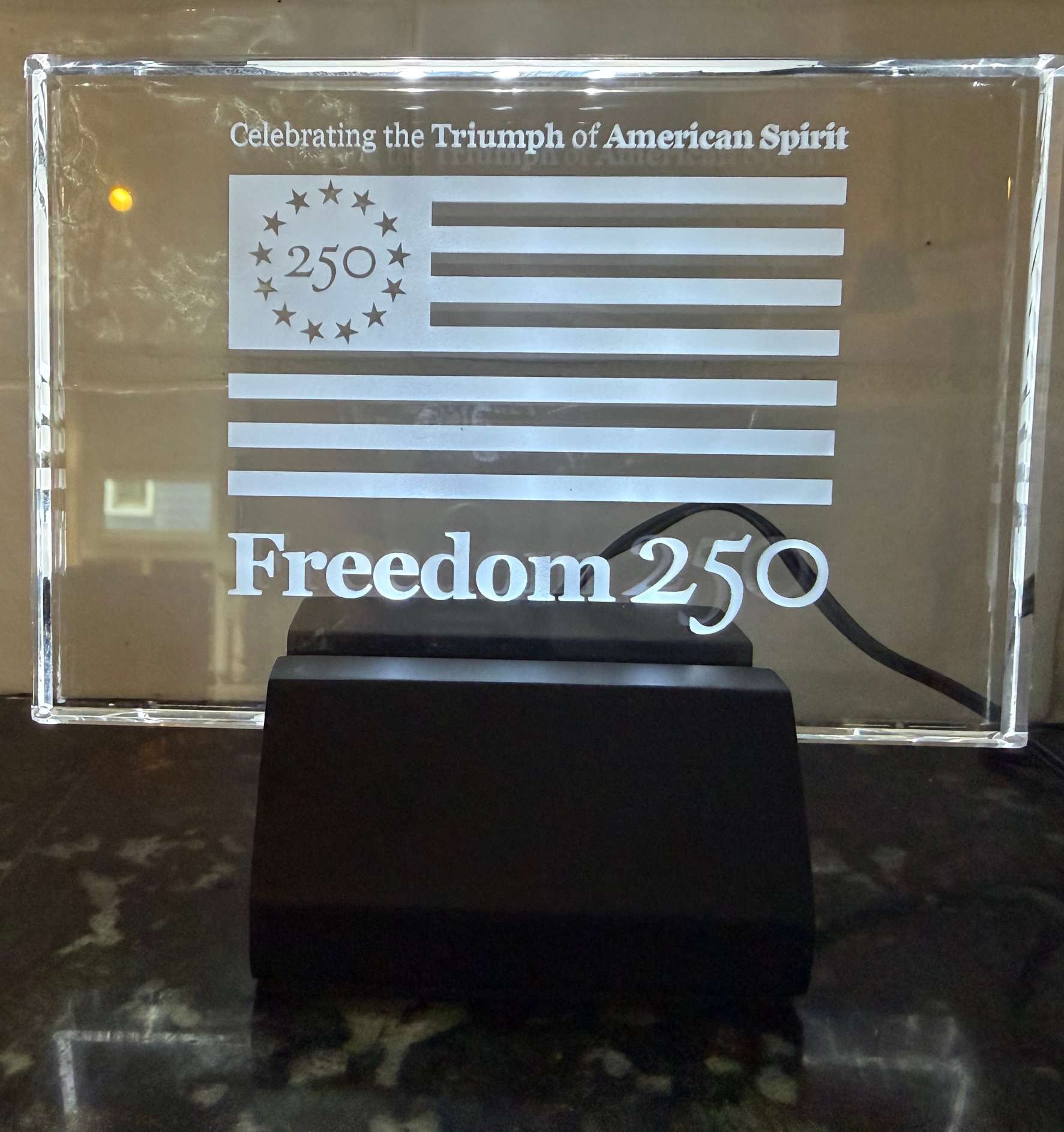 Decorative plaque with American flag design and 'Freedom 250' text on a reflective surface.