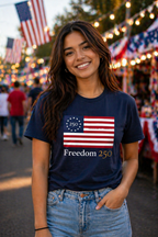 Woman wearing a navy blue t-shirt with a flag design and 'Freedom 250' text, standing in a festive outdoor setting with American flags.