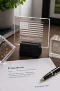 Glass plaque with 'Freedom 250' on a desk with a pen and paper.