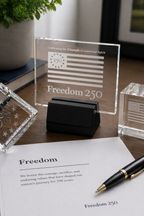 Glass plaque with 'Freedom 250' on a desk with a pen and paper.
