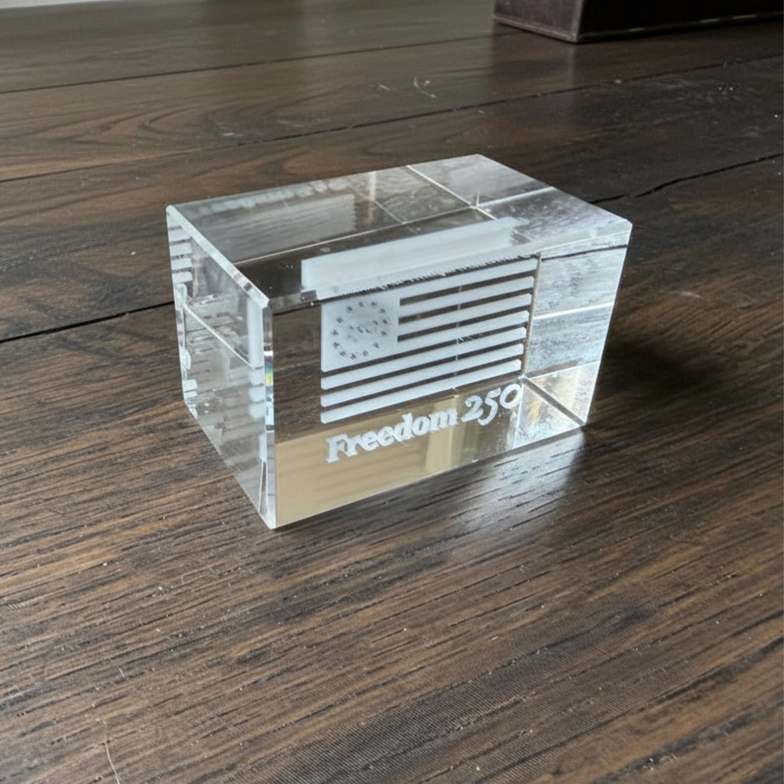 Clear glass block with 'Freedom 250' engraving on a wooden surface
