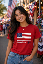 Woman wearing a red t-shirt with 'Freedom 250' design in an outdoor setting with flags.