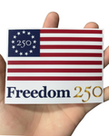Sticker with American flag design and 'Freedom 250' text held between fingers