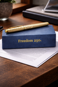 Gold pen on a blue 'Freedom 250' box on a wooden surface
