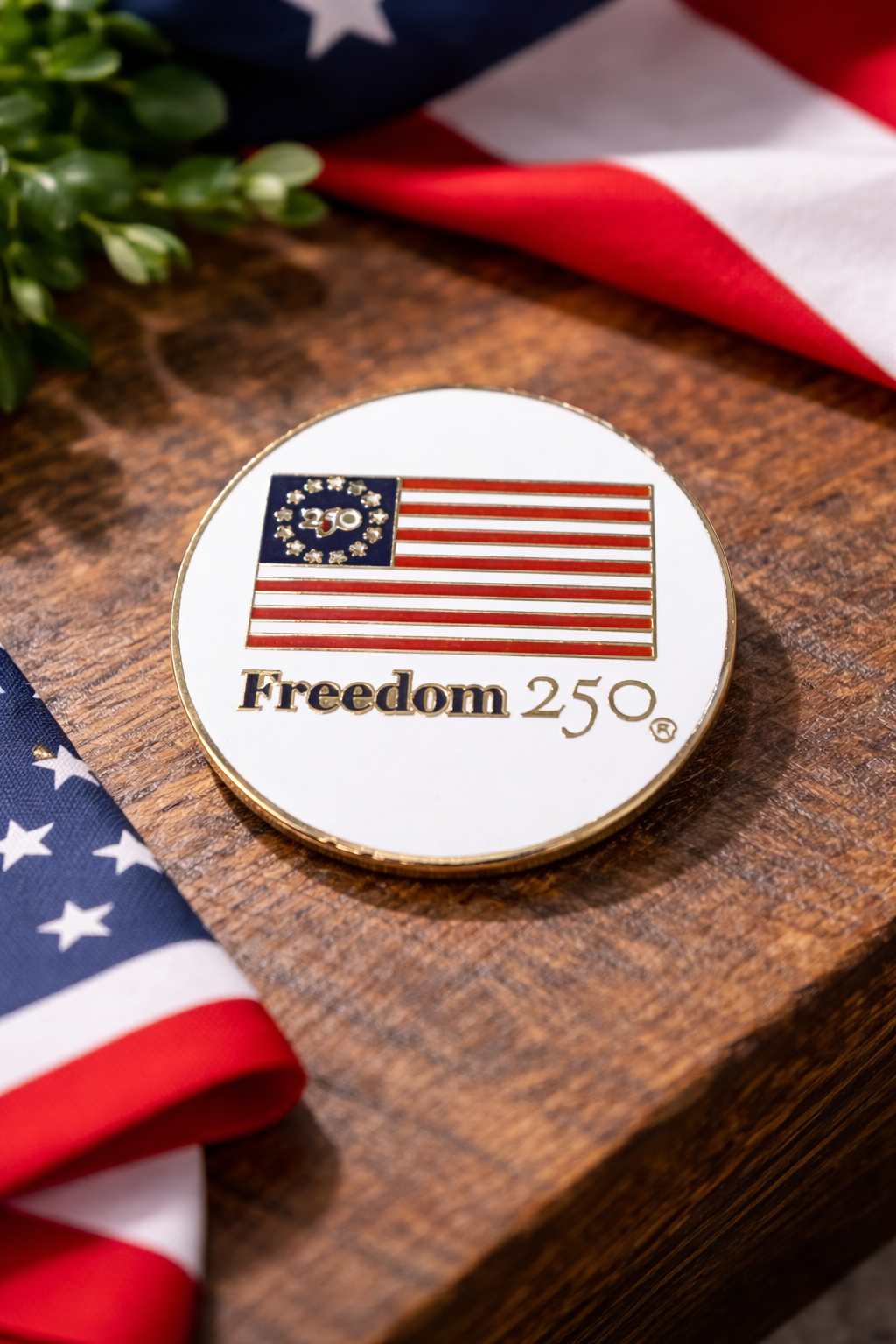 Coin with American flag design and 'Freedom 250' text on a wooden surface with American flags.
