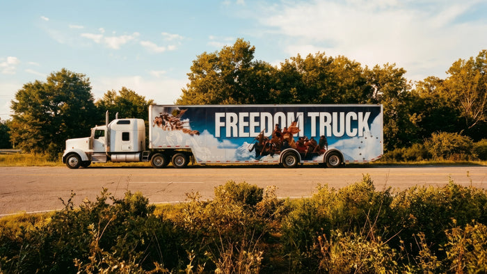 Truck with 'Freedom Truck' on a road surrounded by trees