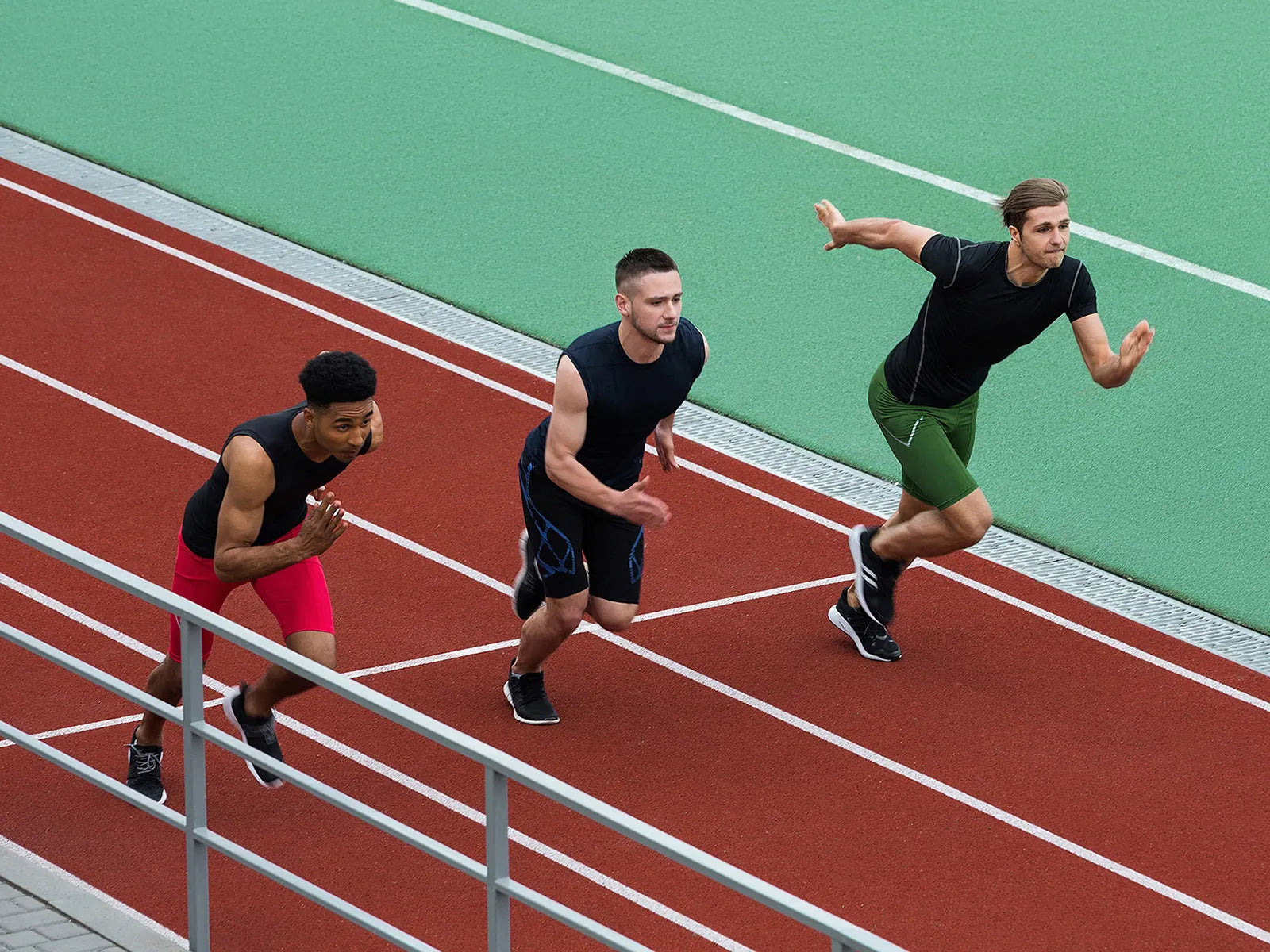 Three athletes running on a track with green and red surface