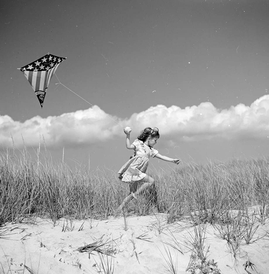 Black and white photo of a girl running on a beach with a kite