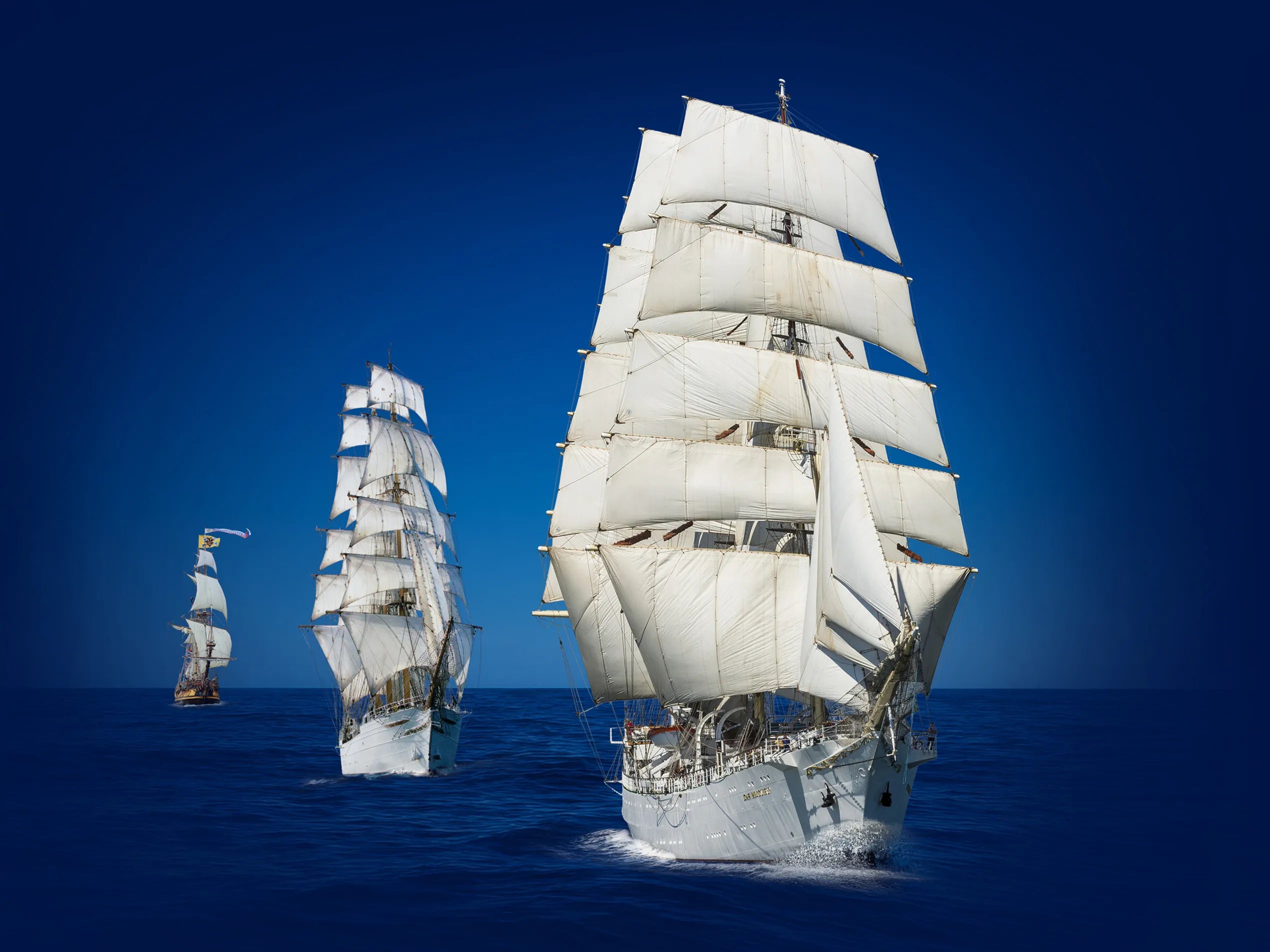 Three large sailing ships with white sails on a blue ocean under a clear sky.